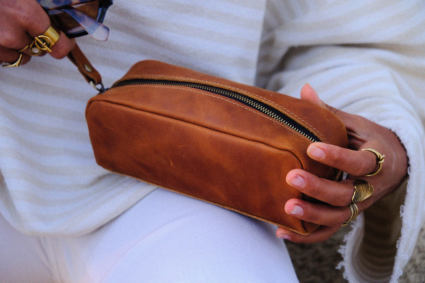 COFFT Latte leather pouch held against a white outfit, showing compact shape and warm tan leather finish