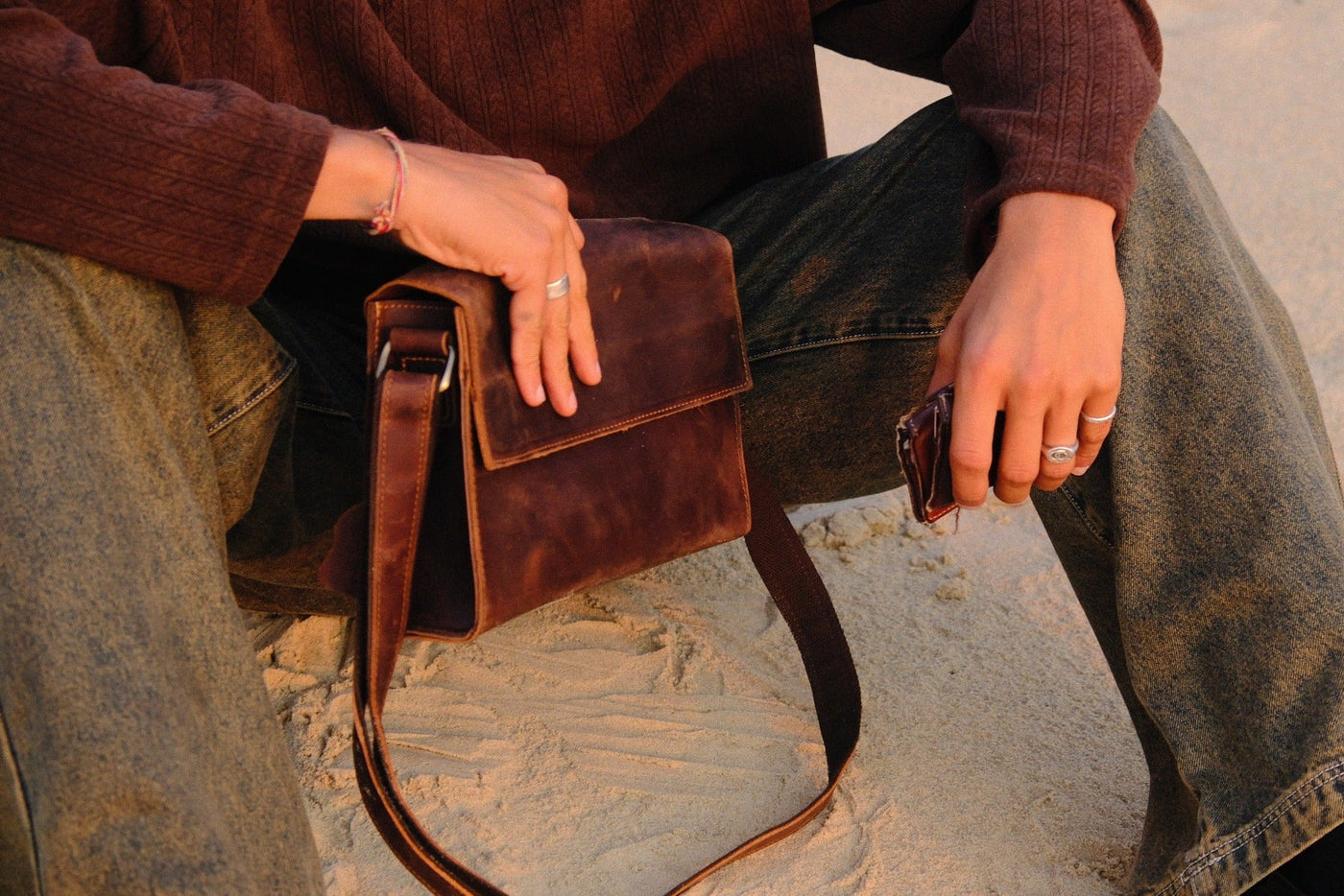 COFFT Espresso leather messenger bag styled in a seated beach lifestyle scene with warm evening light
