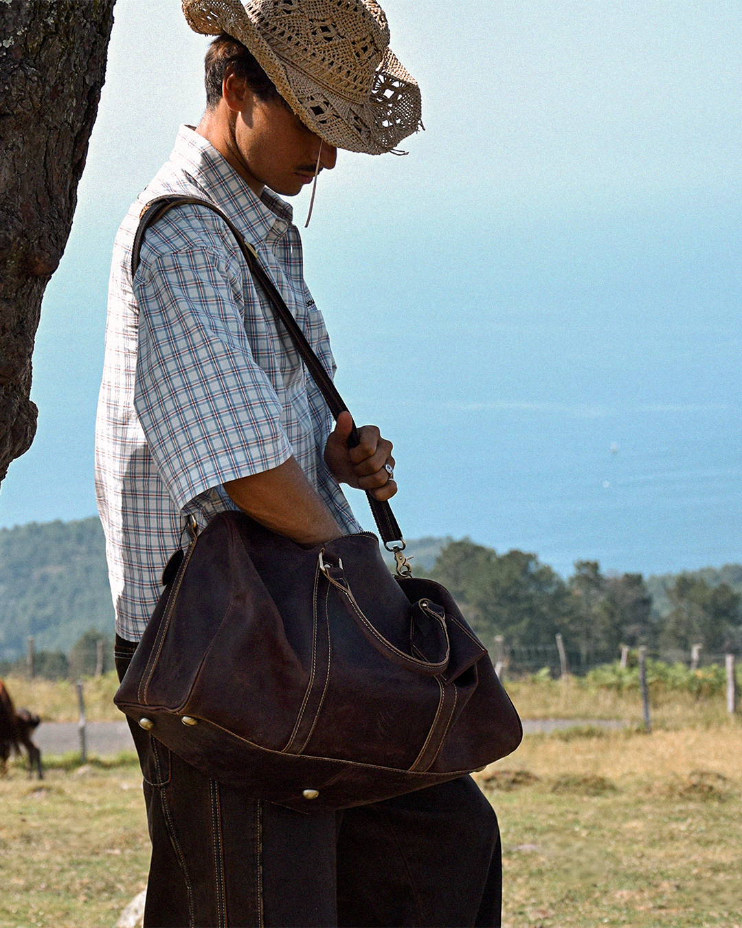 Man in a straw hat carrying the COFFT Signature Patchwork Duffle in Espresso, SS26 Free Like a Horse campaign